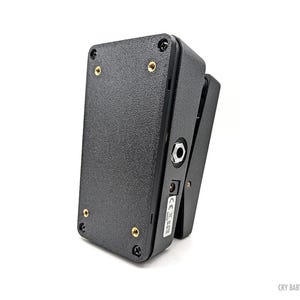 May include: A black Cry Baby Mini guitar effects pedal. The pedal has a textured surface, gold screws, and a jack input. The pedal is angled slightly, showing the side with the input and output jacks.