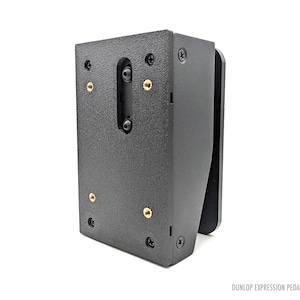 Könnte beinhalten: Schwarze Metallhalterung mit Befestigungsmaterial. Die Halterung hat eine strukturierte Oberfläche und verfügt über mehrere Schrauben und goldfarbene Einsätze. Der Text "DUNLOP EXPRESSION PEDAL MINI" ist unten rechts sichtbar.