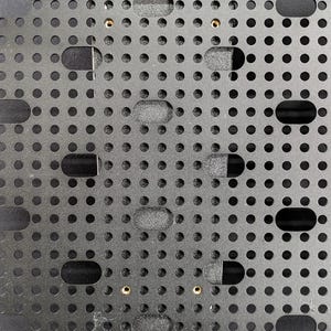 May include: A black metal plate with a grid of evenly spaced holes. The plate has two gold screws in the centre.