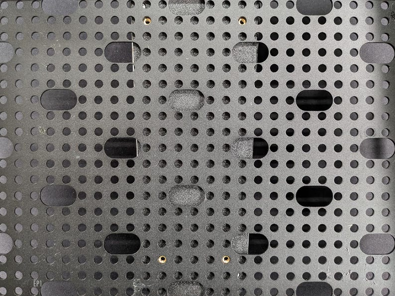 May include: A black metal plate with a grid of evenly spaced holes. The plate has two gold screws in the centre.
