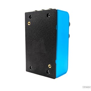 Peut inclure: Vue arrière d'une pédale d'effets Strymon Single bleue et noire. La pédale a une plaque métallique noire avec quatre vis et deux prises de couleur or.