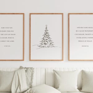 Puede incluir: Tres impresiones enmarcadas con marcos de madera. La impresión de la izquierda tiene texto de Lucas 2:11, la impresión central presenta un boceto de un árbol de Navidad y la impresión de la derecha tiene texto de Isaías 9:6. Las impresiones están sobre un sofá blanco.