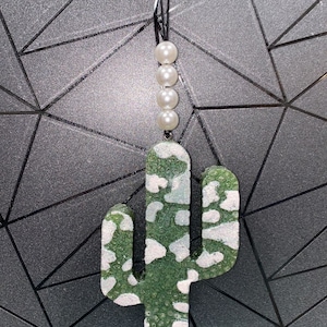 May include: A green and white cactus-shaped car air freshener with a string of white pearls hanging from the top.