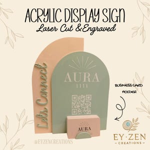 May include: An arched acrylic display sign featuring a peach-colored back panel and a sage green front panel. The front panel displays the text AURA 1111, a QR code, and the words Let's Connect. A matching sage green business card holder is attached.