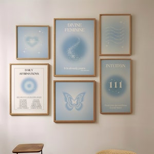May include: A set of six framed prints with blue and white designs. The prints feature affirmations, the divine feminine, intuition, and a butterfly. The prints are hung on a white wall with a wooden floor.