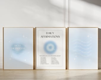 May include: Three framed prints with a blue background and white text. The center print says "Daily Affirmations" and has a list of positive affirmations. The left print says "Trust the Process" and has a circle with stars around it. The right print says "Choose your highest dreams" and has a curved line with stars around it.