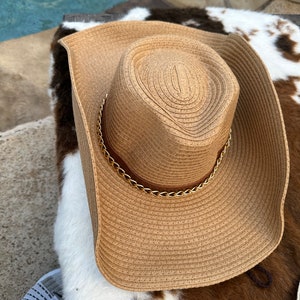 May include: A wide-brimmed straw hat with a gold chain detail around the crown. The hat is brown and has a woven texture.