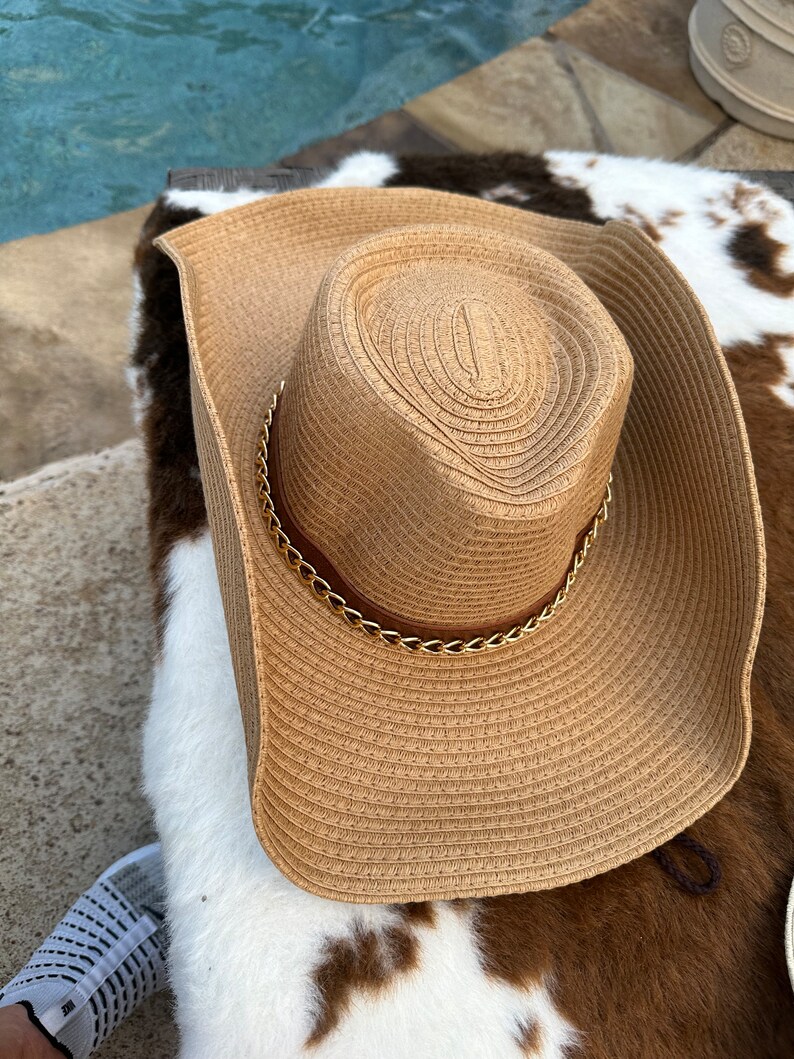 May include: A wide-brimmed straw hat with a gold chain detail around the crown. The hat is brown and has a woven texture.