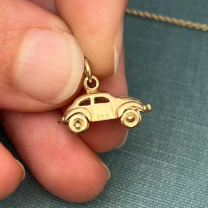 Può includere: Un ciondolo a forma di auto color oro dal design classico. Il ciondolo è sospeso a una catena d'oro ed è tenuto tra le dita. Il ciondolo a forma di auto ha un aspetto dettagliato, con ruote e finestre visibili. Il ciondolo è contrassegnato con "14K".