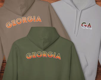 Könnte beinhalten: Drei Kapuzenpullover in Taupe, Olivgrün und Grau. Jeder zeigt das Wort "GEORGIA" oder die Buchstaben "GA" in einem farbenfrohen, strukturierten Design. In der unteren rechten Ecke steht der Text "@TROUTSTATELINES".
