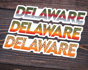 Könnte beinhalten: Drei Aufkleber-Designs mit dem Wort "DELAWARE" in einem weißen Umriss mit einem Hintergrund aus braunen, orangefarbenen, gelben, grünen und blauen Forellenschuppen. Die Aufkleber sind übereinander auf einer braunen Holzoberfläche gestapelt. Der Text "@TROUTSTATELINES" befindet sich am unteren Rand des Bildes.