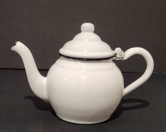 Tetera vintage de esmalte blanco con borde negro, tapa de metal esmaltado con bisagra, estilo rústico campestre, de aproximadamente 15 cm de altura.