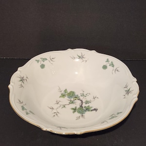 Op de afbeelding: Witte porseleinen serveerschaal met een geschulpte rand en gouden rand. De schaal heeft een bloemenontwerp met groene en grijze bladeren en bloemen. Een klassiek tafelstuk.