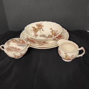 May include: A set of vintage brown and white porcelain dishes with a woodland scene. The set includes a large bowl, two plates, a creamer, and a sugar bowl.