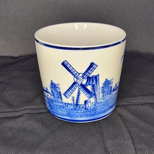 May include: A white ceramic mug with a blue and white windmill design. The mug features a traditional Dutch windmill scene with a blue and white colour scheme.