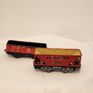 May include: Two vintage toy train cars. One is red and black with "SEA BOARD" and numbers. The other is red with "SOUTHERN" and the number 7461890. Both have black wheels and are on a white surface.