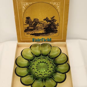 May include: A round, olive green glass serving tray with a scalloped edge and a central starburst pattern, presented in a tan cardboard box labelled Fairfield with a black and white illustration of a house and trees on the lid.