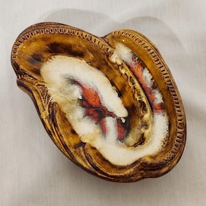 May include: A brown and white ceramic ashtray with a swirl design. The ashtray has a raised rim and a scalloped edge.
