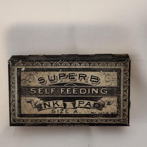 May include: Rectangular ink pad tin with the words "SUPERB SELF FEEDING INK PAD SIZE A" in black and white. The tin has a decorative border and the patent date of Mar. 18, 1901.