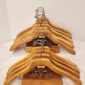 May include: A set of light brown wooden suit hangers with curved shoulders and metal swivel hooks. Each hanger features a horizontal wooden bar with metal clips for trousers. The word Sears is embossed on the bottom wooden bar of the hangers.