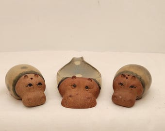 May include: A set of three ceramic hippopotamus-shaped items including two shakers and one central dish. Each piece features a natural terracotta-colored head with painted eyes and a smooth, speckled beige and blue glazed body finish.