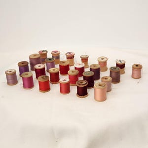 Sortiment av träspolar av 25 merceriserade bomullstrådar. Tillverkad i USA. Lila röd rosa. Ca 3,8 cm hög, ny och begagnad, många nästan fulla.