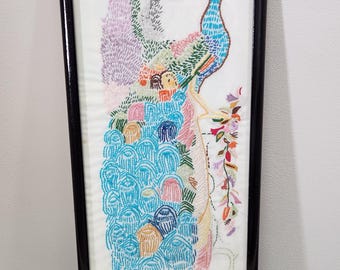 May include: Embroidered peacock art in a black frame. The artwork features a colorful peacock with a blue body, a turquoise tail, and a detailed design. The background includes various colors and textures, creating a vibrant and artistic piece.