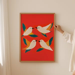 May include: A framed print with a red background and four white birds with yellow and green accents flying in different directions.