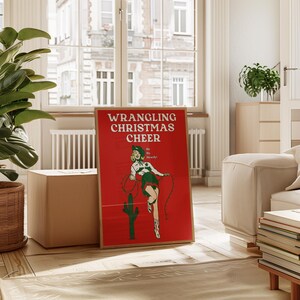 May include: A red poster with a white border featuring a woman in a green and white outfit holding a lasso. The text on the poster reads "WRANGLING CHRISTMAS CHEER" and "Hi Ho Hoardy!"