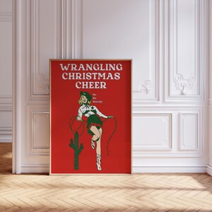May include: A red poster with the text "WRANGLING CHRISTMAS CHEER" in white. A woman in a green and white outfit is lassoing a cactus. The text "Ho Ho Howdy!" is below the woman.