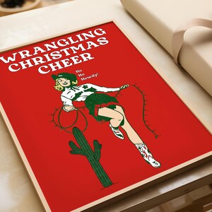 May include: A red poster with the text "WRANGLING CHRISTMAS CHEER" in white. A woman in a cowboy hat and boots is lassoing Christmas lights while riding a cactus. The text "Ho Ho Howdy!" is in green.