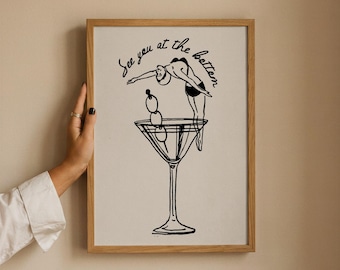 Op de afbeelding: Een ingelijste kunstprint met een zwarte lijntekening van een persoon die in een groot martiniglas vol met drie olijven duikt. De tekst "See you at the bottom" staat in cursief schrift boven de illustratie van het martiniglas.