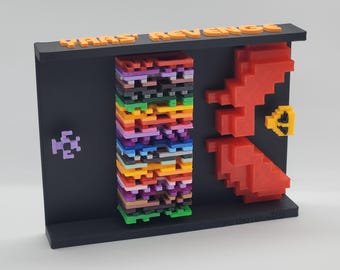 May include: A 3D printed model of the classic arcade game Yars' Revenge. The model features a black base with the game's title in orange letters. The game's iconic spaceship is represented in a stack of colorful blocks, and the enemy Yar is depicted in red blocks. The model includes a small purple spaceship and a gold trophy.