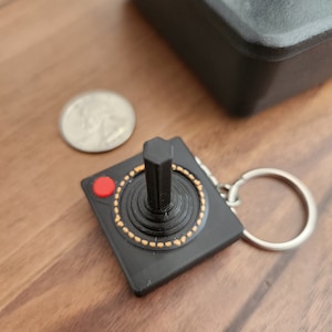 May include: Black plastic keychain shaped like a vintage joystick with a red button and a silver key ring.