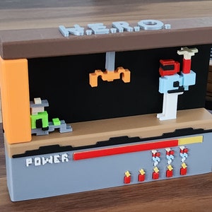 Peut inclure: Modèle 3D imprimé d'une scène de jeu vidéo rétro. La scène présente un personnage pixélisé, une plateforme et un compteur de puissance. Le modèle est peint dans différentes couleurs, notamment l'orange, le vert, le rouge et le bleu. Le modèle est intitulé "HERO" et "POWER".