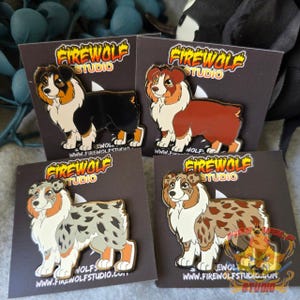 Könnte beinhalten: Vier Emaille-Pins mit Cartoon-Australian-Shepherd-Hunden in verschiedenen Farbvarianten. Die Pins befinden sich auf einem schwarzen Hintergrund mit dem Text "FIREWOLF STUDIO" und einer Website-Adresse.