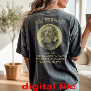 Puede incluir: Camiseta gris oscuro con un retrato amarillo de Galileo Galilei en un círculo. El texto en la camiseta dice "GALILEO GALILEI" y "ITALIAN ASTRONOMER, PHYSICIST, ENGINEER, AND POLYMATH." Una persona lleva la camiseta y sostiene una taza.