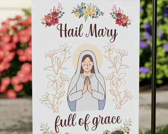 May include: A white garden flag with a floral design and the text "Hail Mary full of grace". The flag features a cartoon image of the Virgin Mary with her hands clasped in prayer.