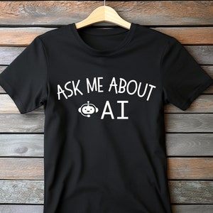 Peut inclure: T-shirt noir avec un texte blanc qui dit "Ask me about AI" et une petite icône de robot.