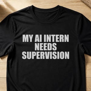 Peut inclure: Un t-shirt noir à manches courtes avec le texte MY AI INTERN NEEDS SUPERVISION imprimé en lettres capitales gris clair sur la poitrine. Le vêtement présente une encolure ronde classique et une coupe droite standard au niveau de l'ourlet.