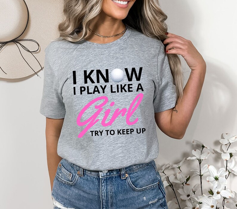 May include: Gray short-sleeved t-shirt with black text that reads "I KNOW I PLAY LIKE A GIRL TRY TO KEEP UP" and a white golf ball graphic. The text "GIRL" is in pink.