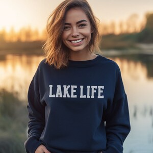 May include: A woman wearing a navy blue sweatshirt with the text "LAKE LIFE" printed in white on the front.