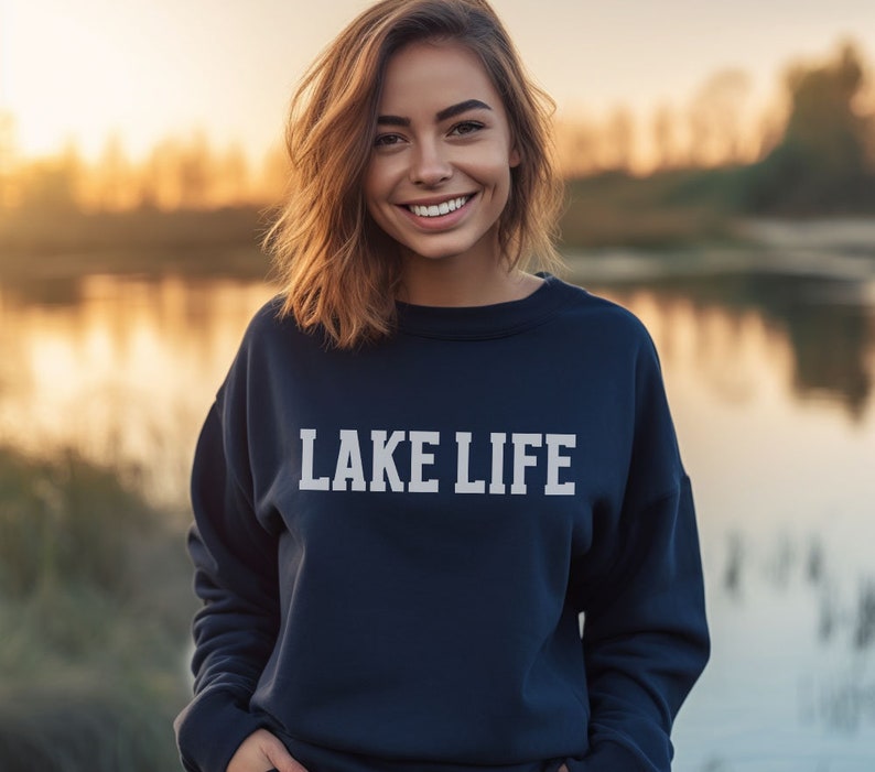 May include: A woman wearing a navy blue sweatshirt with the text "LAKE LIFE" printed in white on the front.