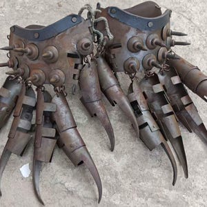 Pu&ograve; includere: Un paio di guanti di metallo usurato con lunghe estensioni curve a forma di artiglio. I guanti sono adornati con rivetti e punte e sono collegati da una corda. Il colore generale &egrave; marrone arrugginito.