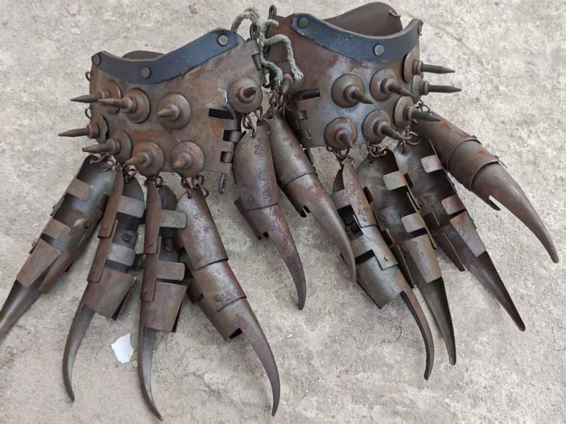 Pu&ograve; includere: Un paio di guanti di metallo usurato con lunghe estensioni curve a forma di artiglio. I guanti sono adornati con rivetti e punte e sono collegati da una corda. Il colore generale &egrave; marrone arrugginito.