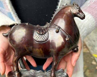 Puede incluir: Una figura de caballo de color bronce con silla de montar y brida. La escultura tiene una melena y cola detalladas, y está montada sobre una base. El caballo es de color marrón oscuro con un acabado pulido.