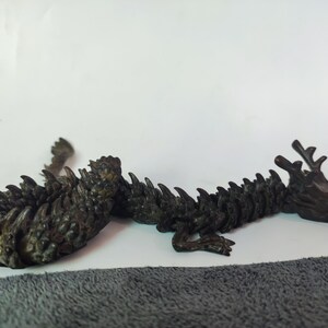 May include: A black dragon figurine with a spiky, segmented body and a detailed head with horns. The dragon is lying on its side with its head turned to the right.