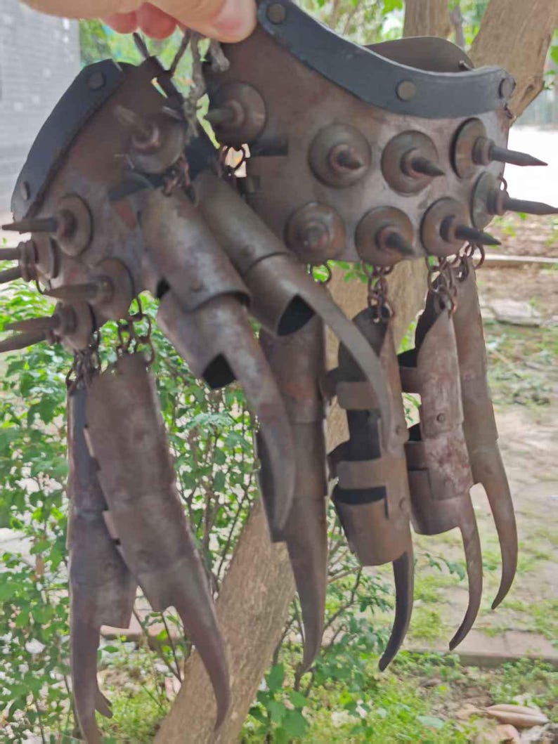 Pu&ograve; includere: Un guanto di metallo arrugginito con lunghe lame ricurve e borchie. Il guanto ha un cinturino in pelle ed &egrave; collegato a diverse lame articolate a forma di dita. Il design suggerisce un'arma o un elemento di costume.