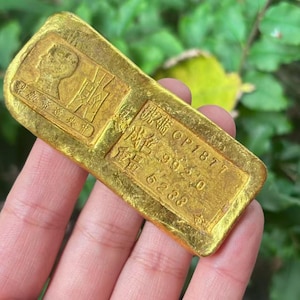 May include: A rectangular gold bar with embossed Chinese characters and a profile image. The bar has a slightly worn appearance. The text includes "OP1877" and weight information.