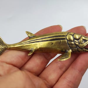 May include: A detailed, brass-colored fish figurine with dark stripes along its body. The fish has an open mouth and detailed fins. The figurine is approximately 5 inches long.